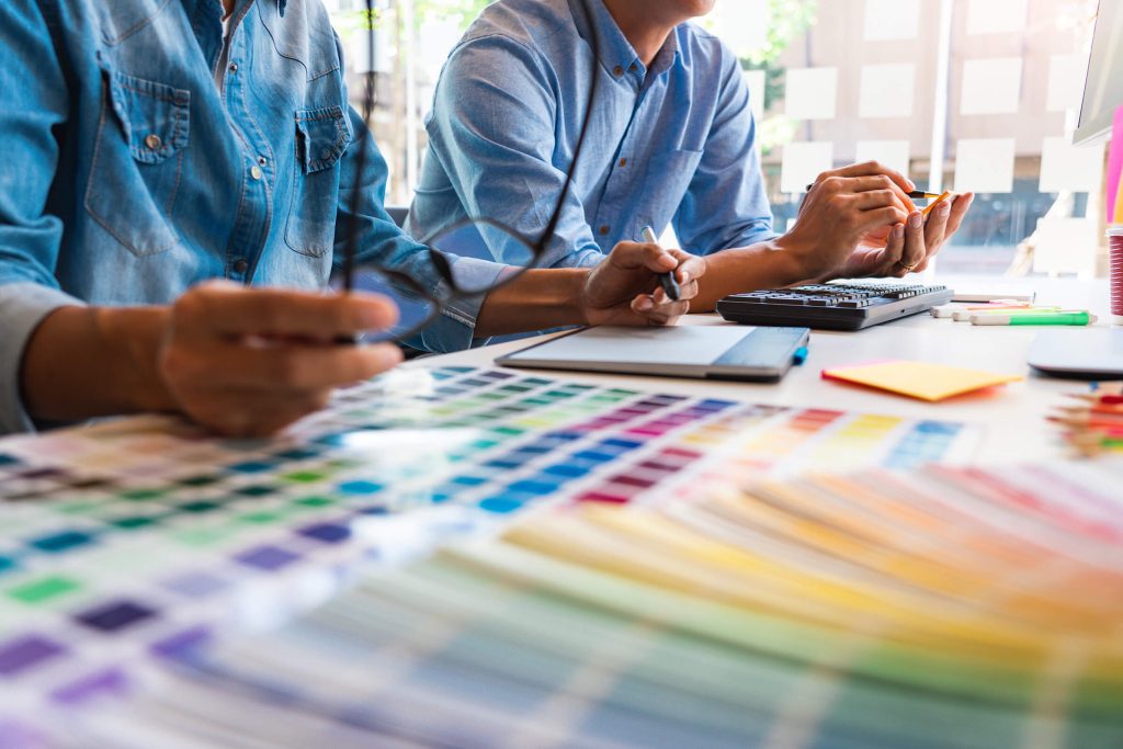 Two people with a color wheel out on a table while drawing on a drawing tablet and discussing creative work